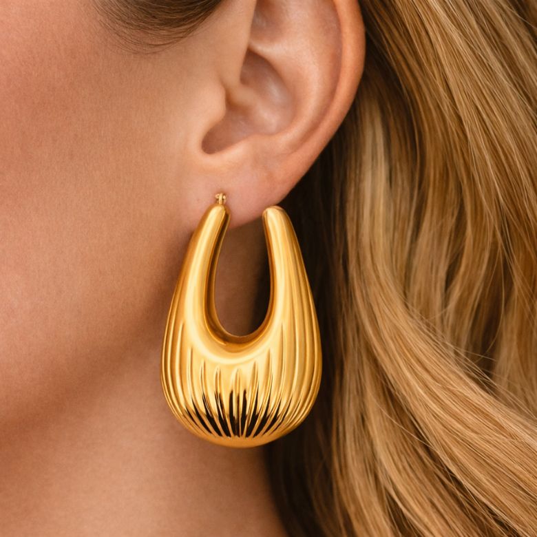 Close-up of a woman wearing Orecchini a Goccia in Acciaio Dorato, gold-tone teardrop earrings with textured detailing and secure snap closure.