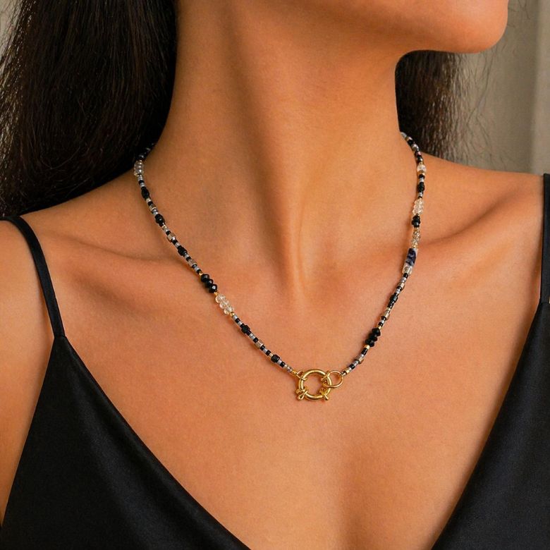 Collana con perline nere, bianche e grigie, chiusura frontale dorata. Elegante collana indossata.