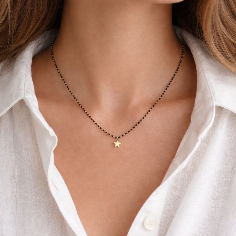 Collana acciaio dorato con sfere nere e stella indossata. Gioiello elegante.
